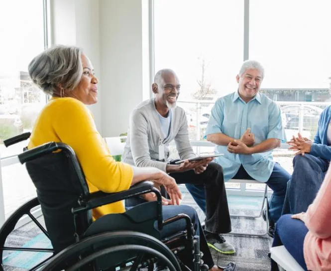 A group of older people, including a wheelchair user, talking together in a bright community room